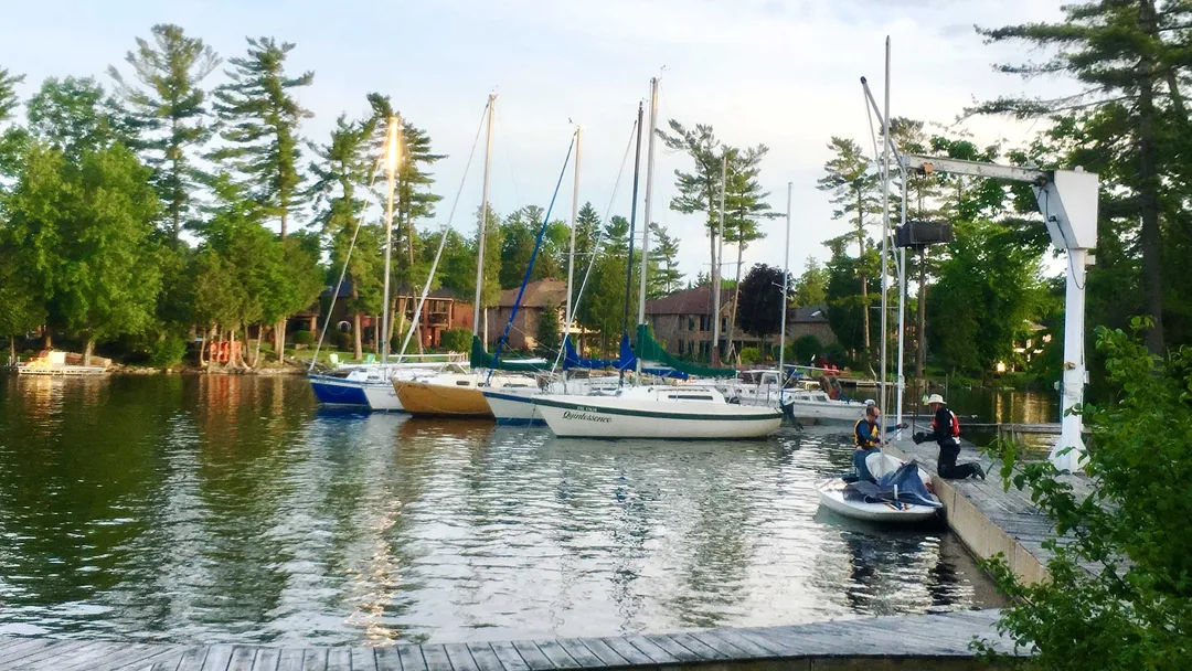 Photo of docks and several sailboats. There are two men preparing to lift a small sailboat out of the water using a hoist.